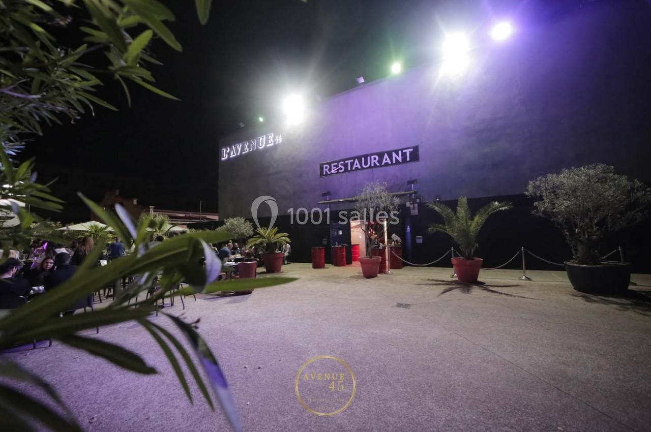 Façade d'un restaurant éclairé de nuit, entourée de plantes en pots sur une terrasse spacieuse.