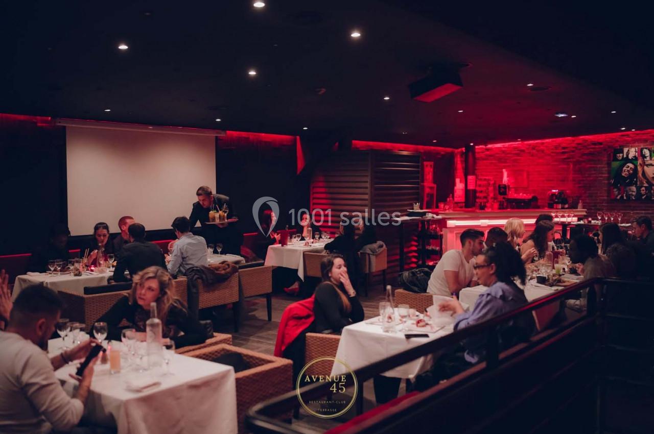 Salle de restaurant animée avec des tables occupées, éclairage tamisé et décor chaleureux.