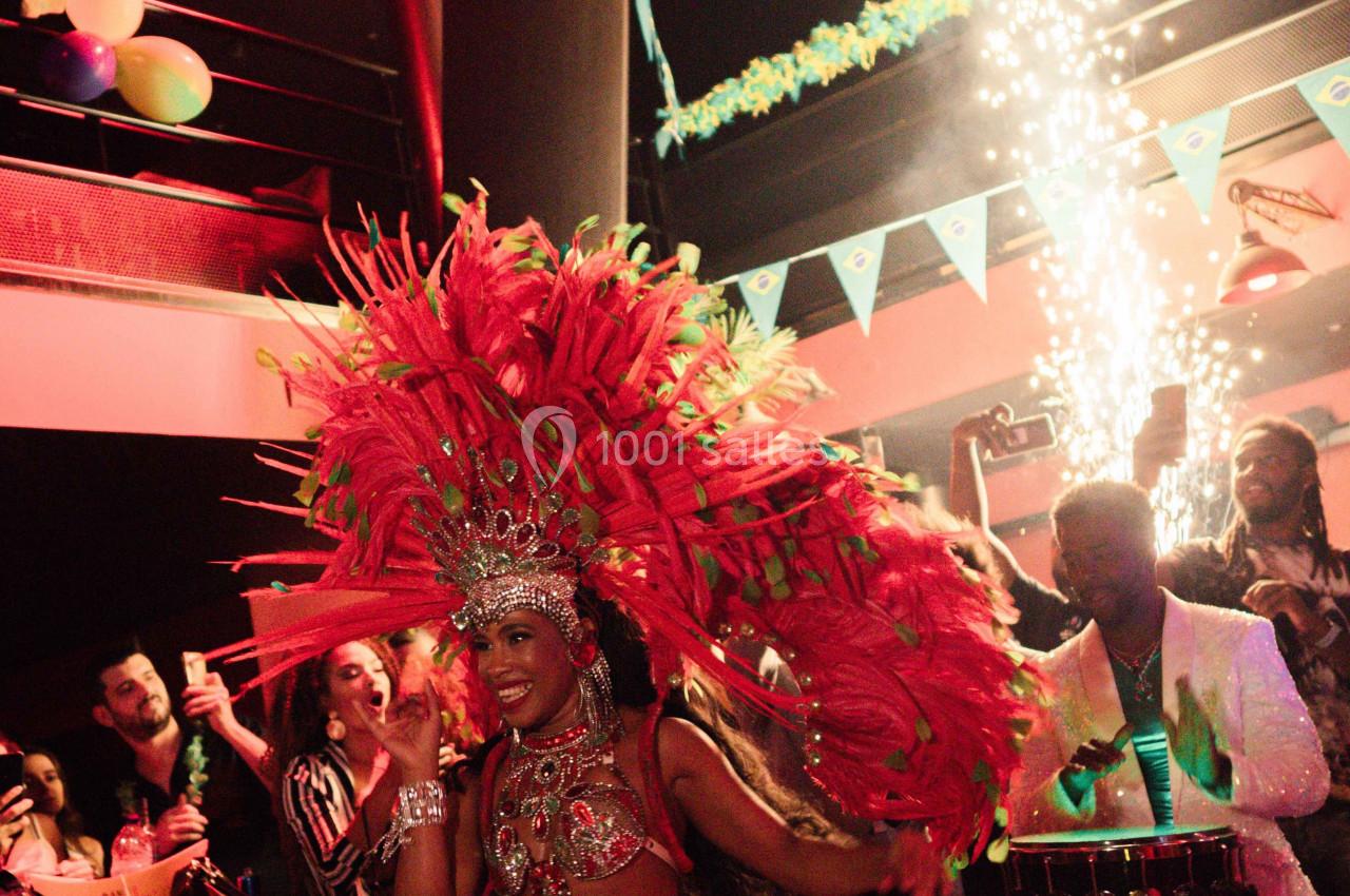 Danseuse en costume de carnaval rouge avec plumes, performe dans une ambiance festive sous des drapeaux brésiliens.