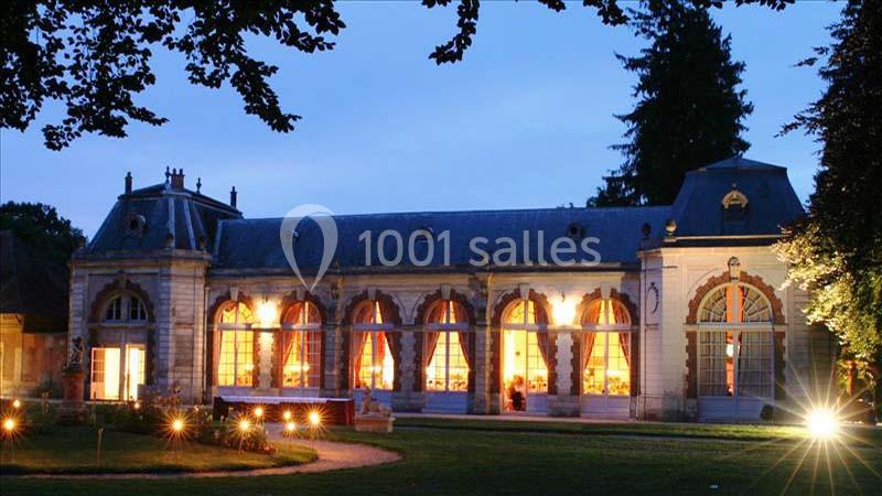 Bâtiment ancien éclairé de nuit, avec de grandes fenêtres en arche laissant entrevoir une lumière chaleureuse.