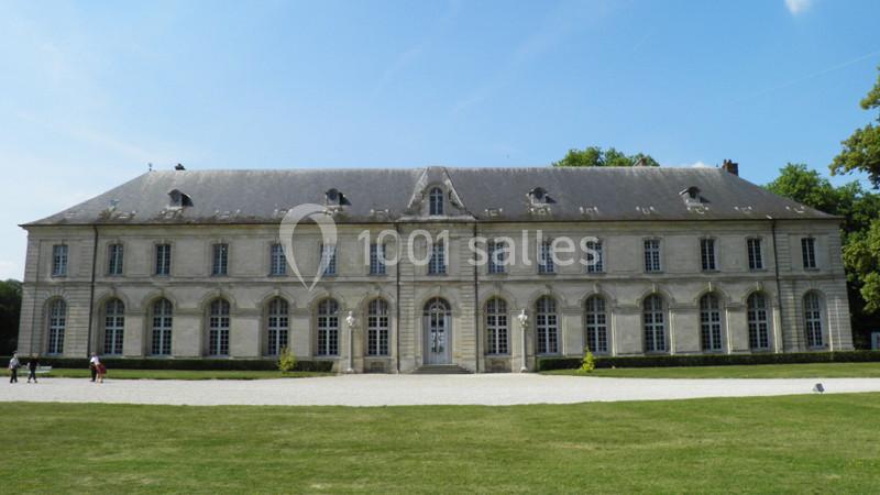 Façade d'un bâtiment historique en pierre avec toit en ardoise, entouré de pelouse et d'arbres.