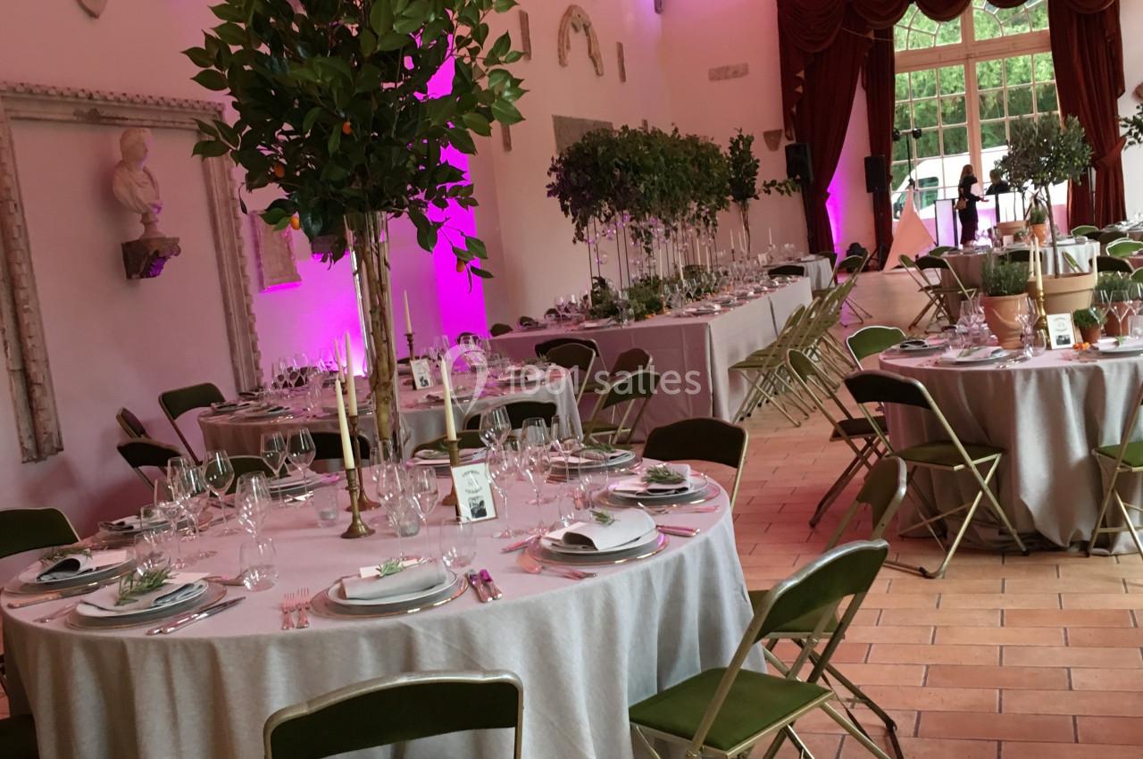Salle de réception décorée avec des tables rondes dressées, chaises vertes et éclairage d'ambiance rose.