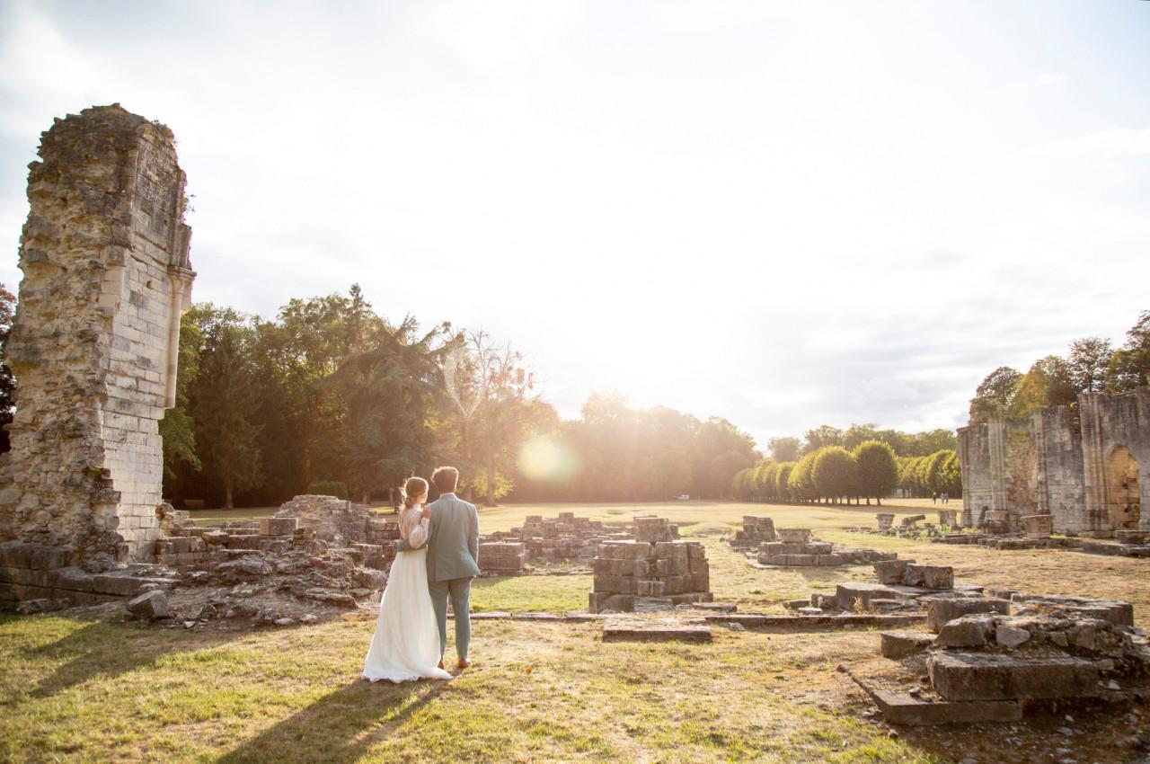 Un couple debout dans les ruines d'une abbaye, regardant un paysage ensoleillé avec des arbres en arrière-plan.