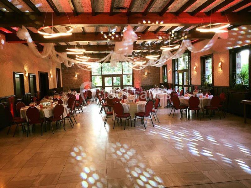 Salle de réception décorée avec des tables rondes dressées, des chaises rouges et des lumières suspendues.