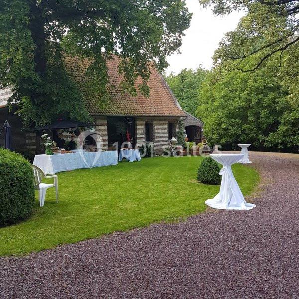 Jardin avec pelouse bien entretenue, tables dressées et maison en briques entourée d'arbres.