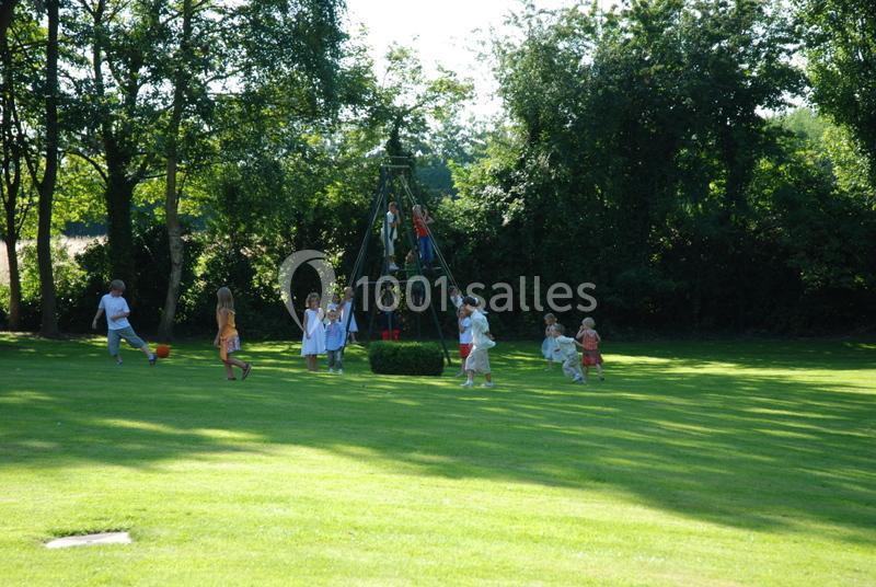 Des enfants jouent autour et sur une structure en bois dans un parc verdoyant par une journée ensoleillée.