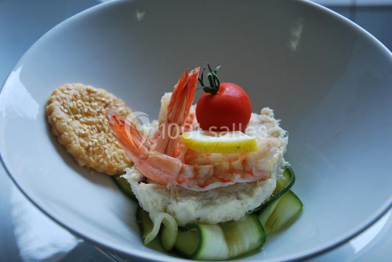 Plat composé de crevettes, rondelle de citron, tomate cerise, courgettes et biscuit salé dans une assiette blanche.