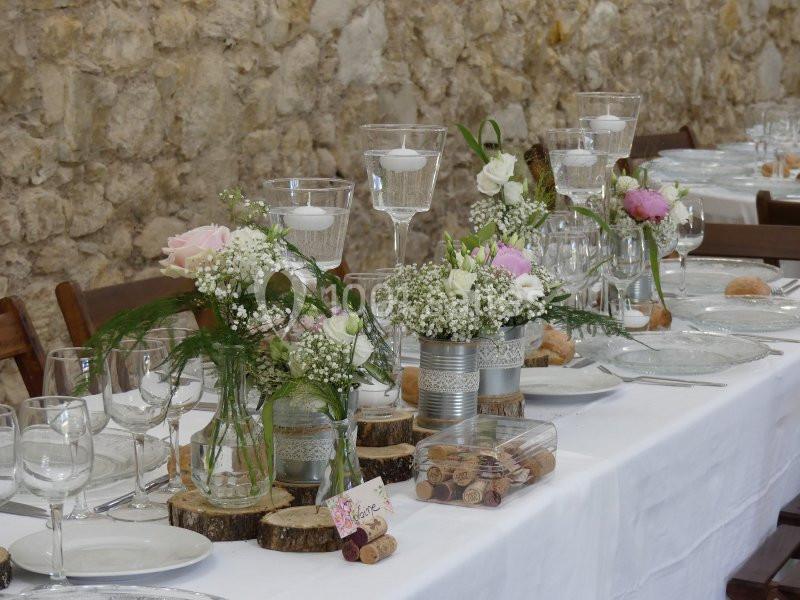 Table décorée pour un mariage avec des fleurs, bougies et éléments rustiques sur une nappe blanche.