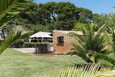 Tente en toile beige installée sur un sol gravillonné, entourée d'arbres, avec des lits aménagés à l'intérieur.