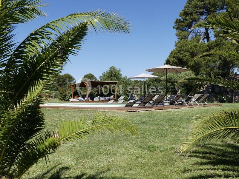 Espace extérieur avec piscine, transats, parasols et pergola, entouré de pelouse et de végétation.