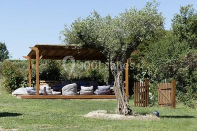 Tente en toile beige installée sur un sol gravillonné, entourée d'arbres, avec des lits aménagés à l'intérieur.