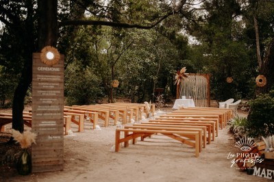 Tente en toile beige installée sur un sol gravillonné, entourée d'arbres, avec des lits aménagés à l'intérieur.