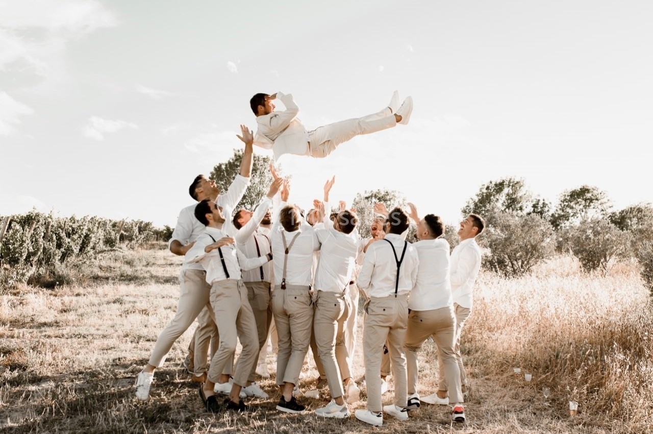 Un groupe d'hommes en tenue claire lance une personne en l'air dans un champ sous un ciel dégagé.
