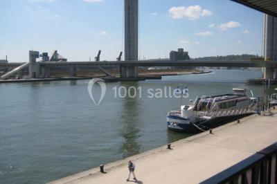 Espace intérieur lumineux avec fauteuils rouges et noirs, tables hautes, plantes et stands d'exposition en arrière-plan.