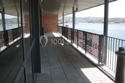Espace intérieur lumineux avec fauteuils rouges et noirs, tables hautes, plantes et stands d'exposition en arrière-plan.