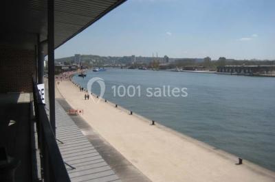 Espace intérieur lumineux avec fauteuils rouges et noirs, tables hautes, plantes et stands d'exposition en arrière-plan.