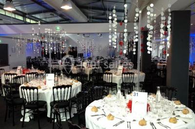 Espace intérieur lumineux avec fauteuils rouges et noirs, tables hautes, plantes et stands d'exposition en arrière-plan.