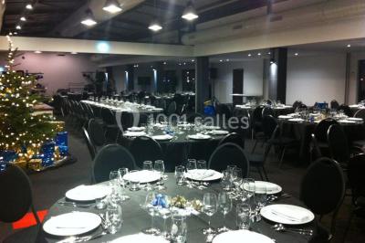 Espace intérieur lumineux avec fauteuils rouges et noirs, tables hautes, plantes et stands d'exposition en arrière-plan.