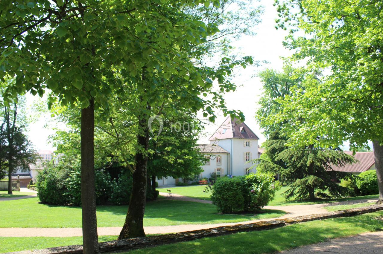 Parc verdoyant avec allées bordées d'arbres et un bâtiment à toit en pente visible en arrière-plan.