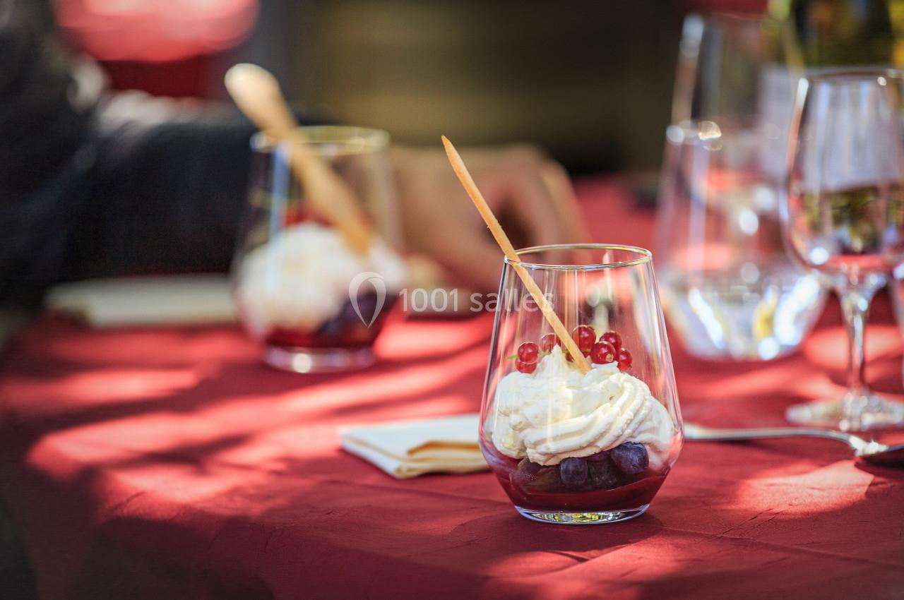 Deux verrines de dessert avec crème fouettée, fruits rouges et cuillère en bois sur une table rouge.