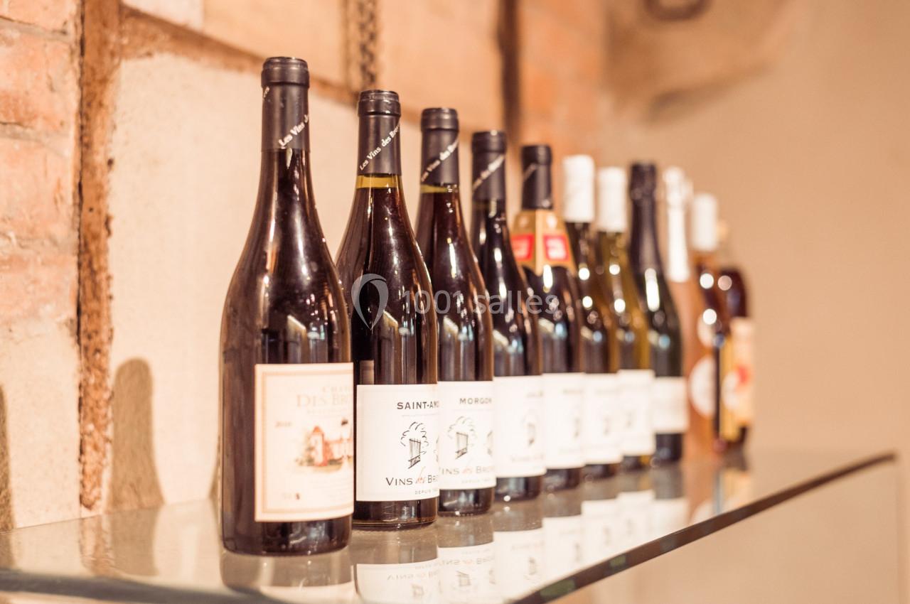 Bouteilles de vin alignées sur une étagère en verre devant un mur en briques.