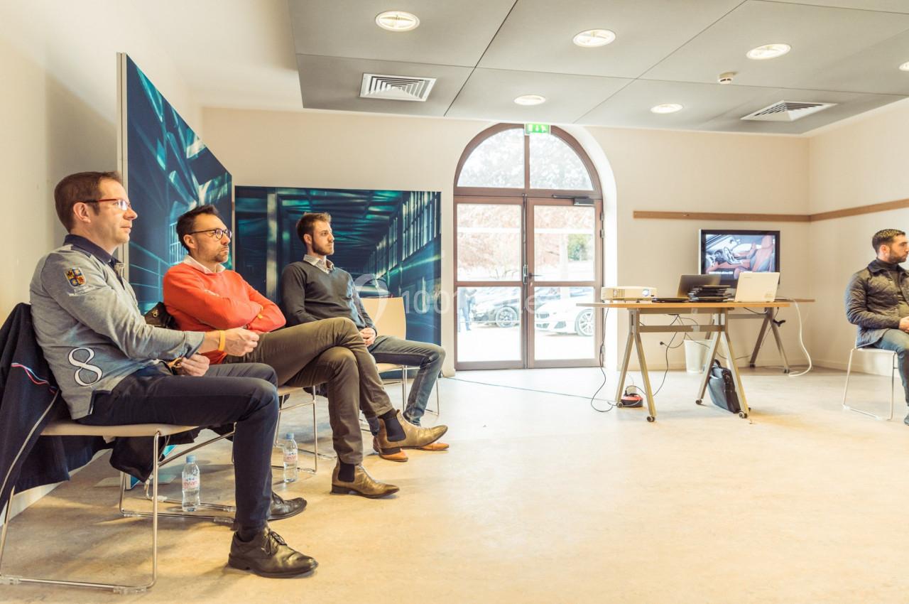 Quatre hommes assis dans une salle lumineuse avec un écran et un projecteur en arrière-plan.