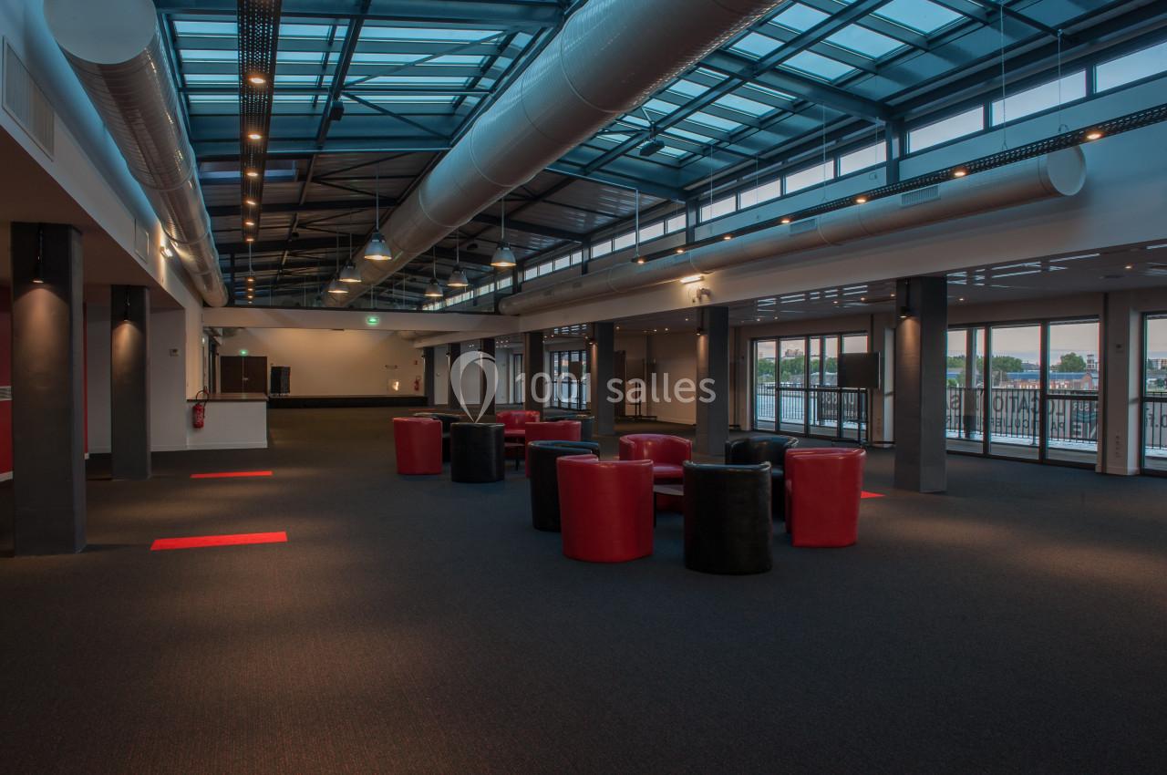 Salle spacieuse avec plafond vitré, mobilier rouge et noir, éclairage artificiel et grandes baies vitrées.