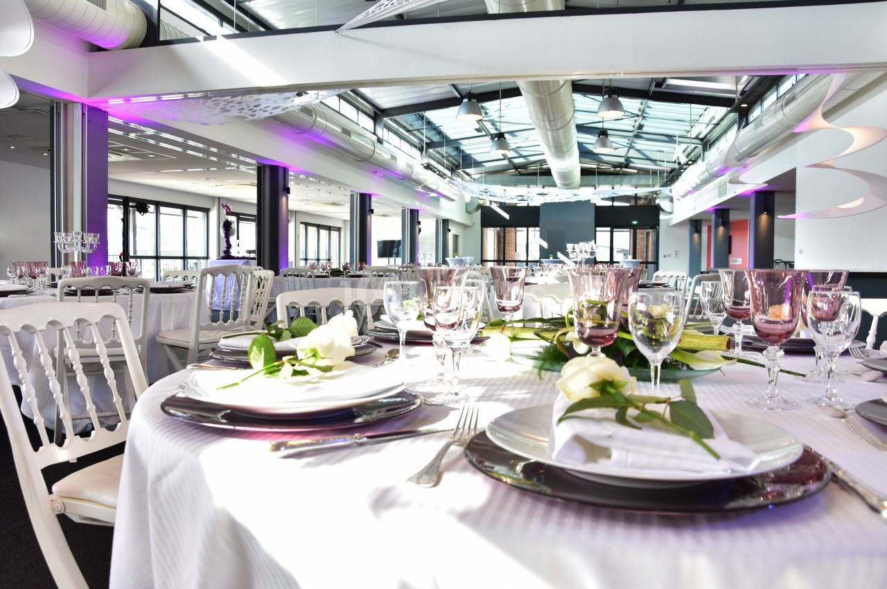 Salle de réception lumineuse avec tables élégamment dressées, décorées de fleurs blanches et vaisselle raffinée.