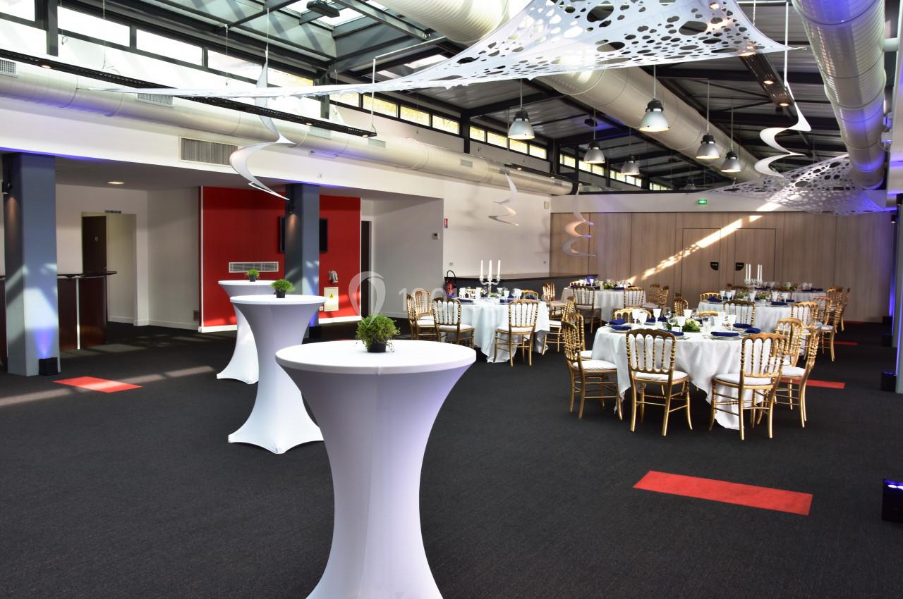 Salle de réception moderne avec tables rondes dressées, chaises dorées et décorations suspendues.