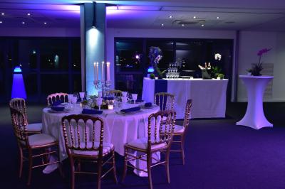 Vue nocturne d'une terrasse éclairée en bleu avec une rivière et un pont illuminé en arrière-plan.