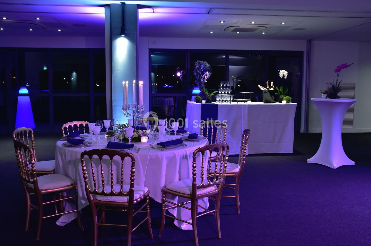 Salle de réception élégamment décorée avec une table ronde dressée, chandeliers et éclairage d'ambiance violet.