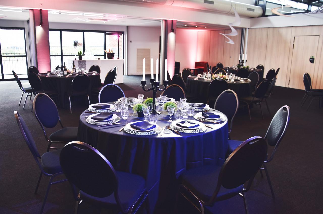 Salle de réception aménagée avec des tables rondes dressées, éclairage tamisé et décoration élégante.