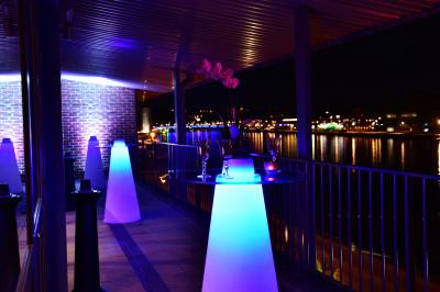 Vue nocturne d'une terrasse éclairée en bleu avec une rivière et un pont illuminé en arrière-plan.