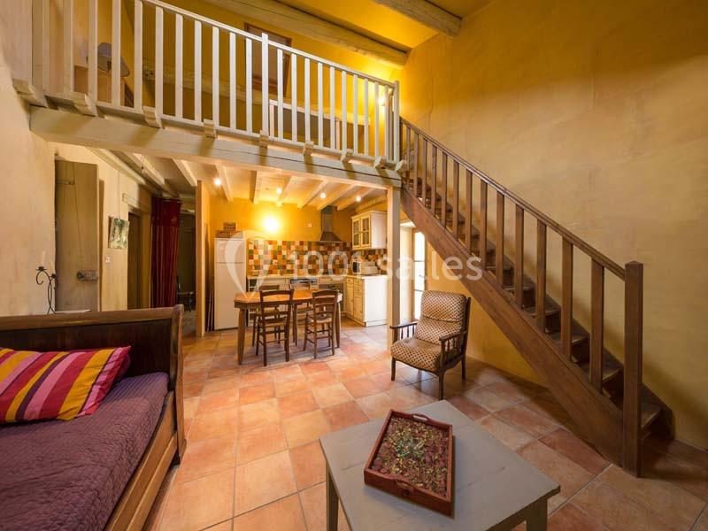Vue d'une pièce avec mezzanine, escalier en bois, cuisine équipée, table à manger et canapé dans un décor chaleureux.