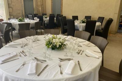 Tables rondes dressées avec nappes blanches et décorations, disposées en extérieur sur une terrasse ensoleillée.