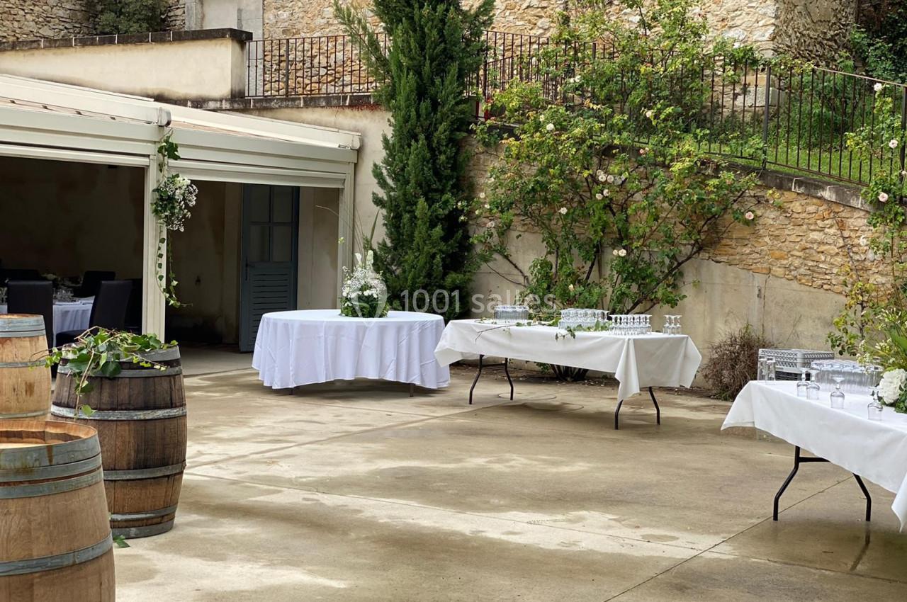 Cour extérieure aménagée pour un événement, avec tables dressées, tonneaux décoratifs et végétation en arrière-plan.