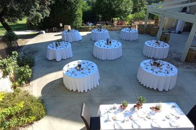 Tables rondes dressées avec nappes blanches et décorations, disposées en extérieur sur une terrasse ensoleillée.