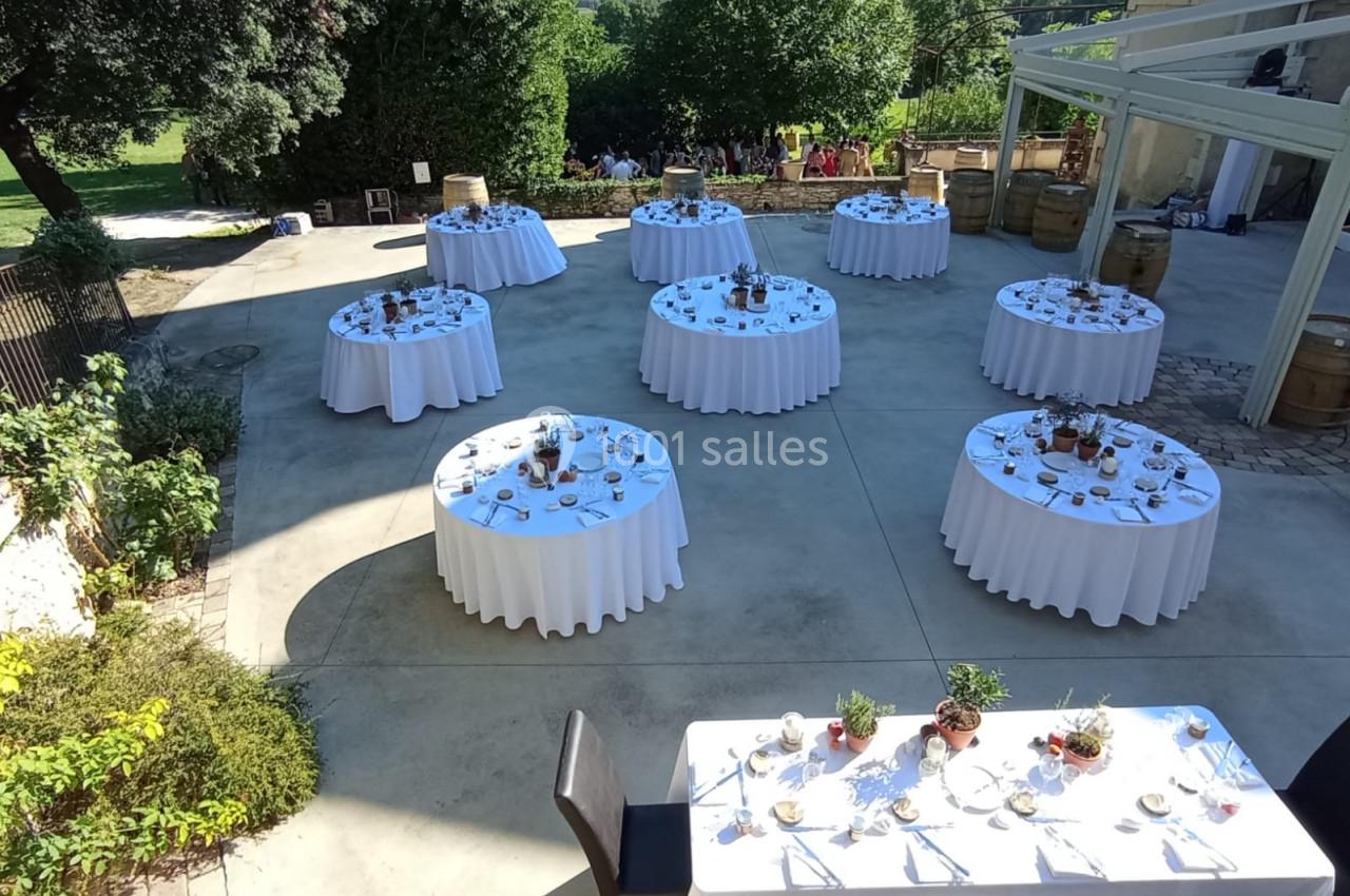 Tables rondes dressées avec nappes blanches et décorations, disposées en extérieur sur une terrasse ensoleillée.