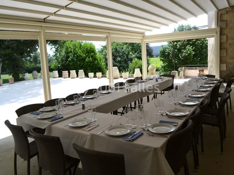 Table dressée pour un repas, avec vaisselle et couverts, sous une pergola ouverte donnant sur un jardin verdoyant.