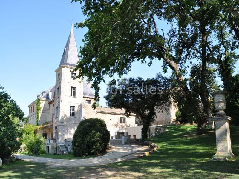 Manoir en pierre avec tour, entouré d'arbres et d'une pelouse, sous un ciel dégagé.