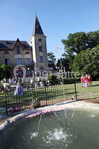 Jardin avec fontaine au premier plan, château en arrière-plan et personnes réunies lors d'un événement en plein air.