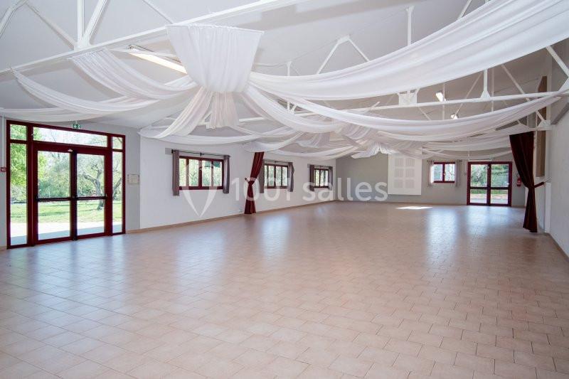 Salle spacieuse avec carrelage clair, grandes fenêtres, rideaux bordeaux et plafond décoré de voilages blancs.