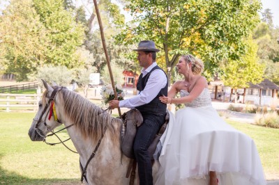 Un couple en tenue de mariage pose devant un groupe de cavaliers alignés sur des chevaux dans un espace verdoyant.