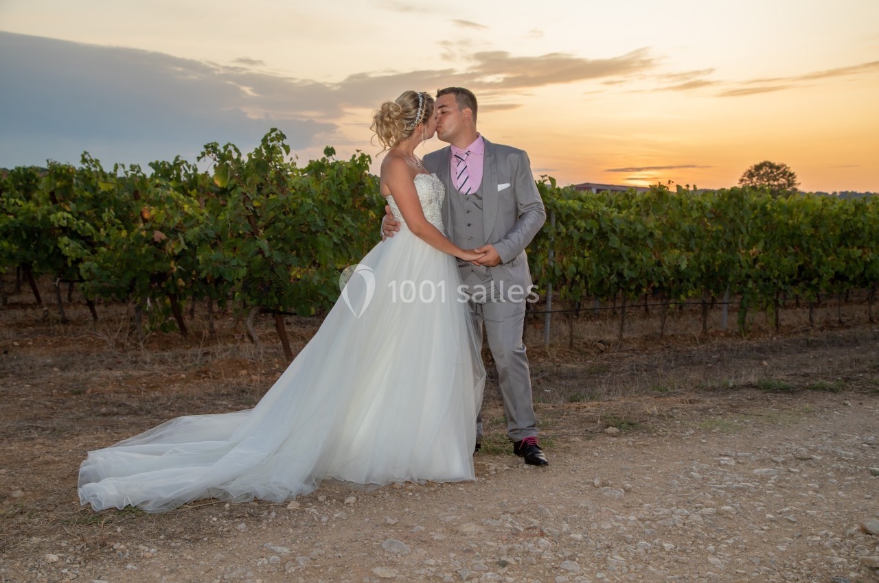 Un couple en tenue de mariage s'embrasse devant un vignoble au coucher du soleil.