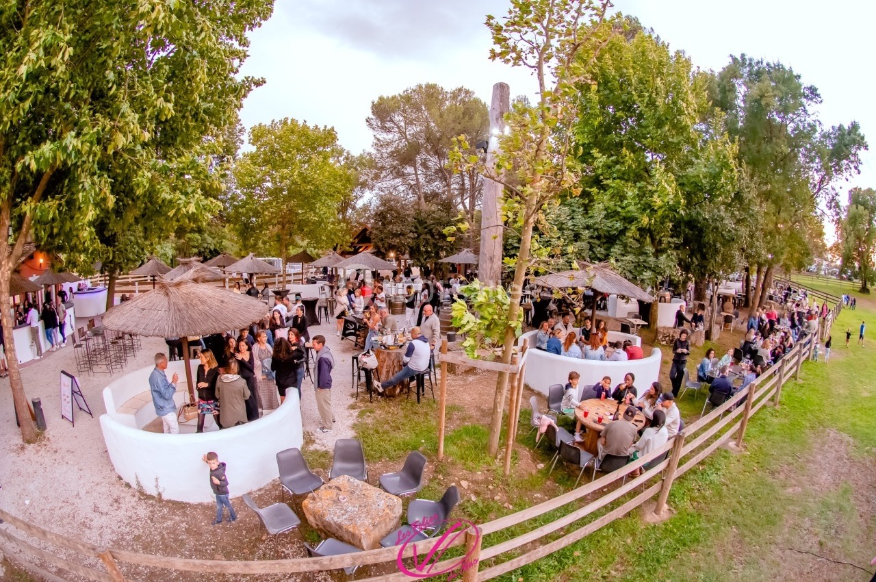 Vue aérienne d'un espace extérieur avec des tables, des parasols en paille et des personnes réunies dans une ambiance…
