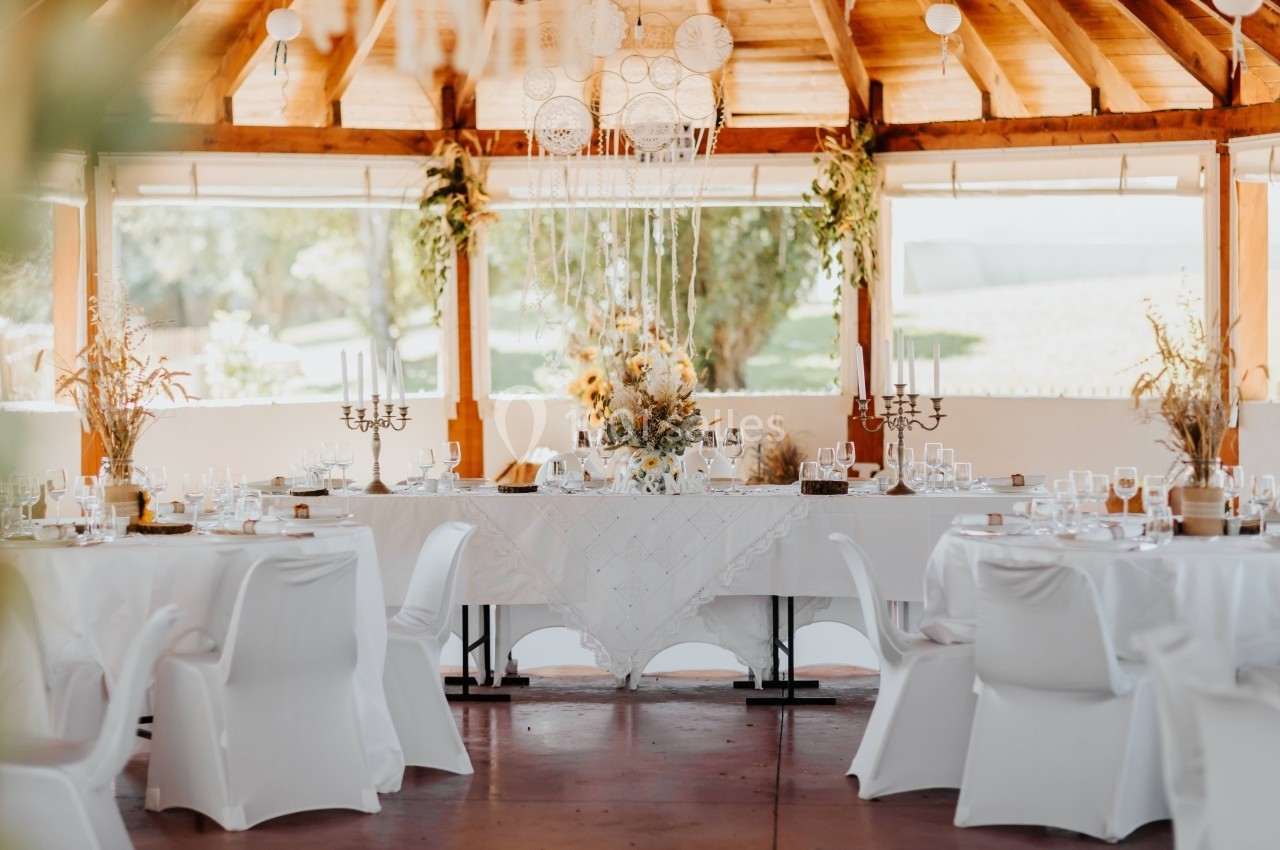 Salle décorée pour un événement avec une grande table dressée, nappes blanches, chandeliers et ornements floraux.