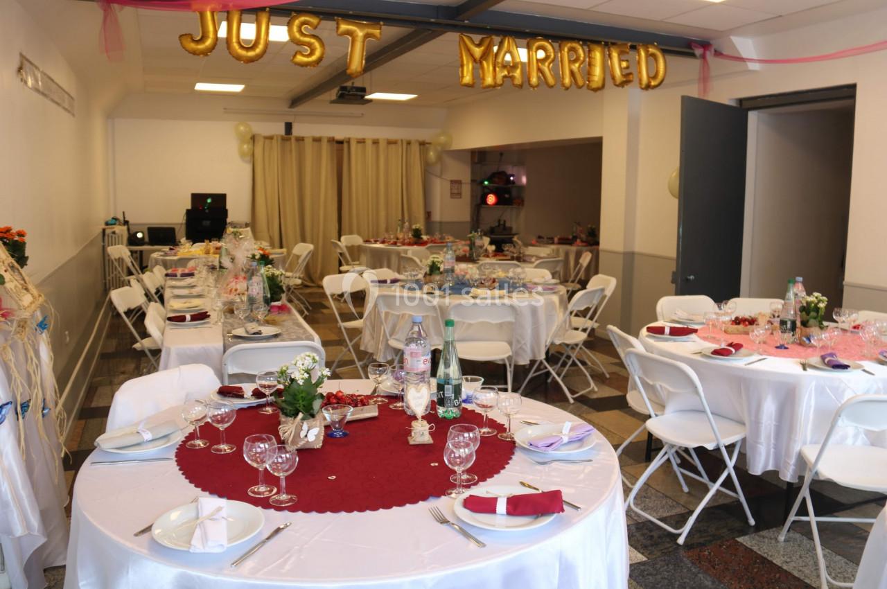 Salle décorée pour une réception de mariage avec tables dressées, nappes blanches et ballons ’Just Married’.