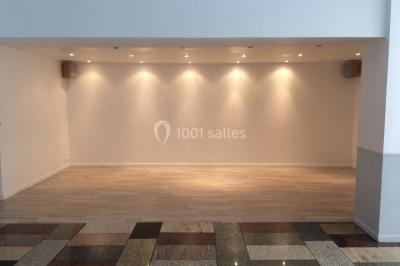 Salle lumineuse avec un grand miroir mural, sol en parquet clair et murs blancs, éclairée par des spots au plafond.