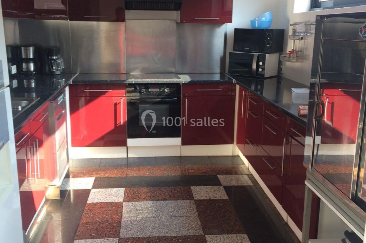 Cuisine moderne avec meubles rouges brillants, plan de travail noir, électroménagers intégrés et sol en carrelage à motifs.