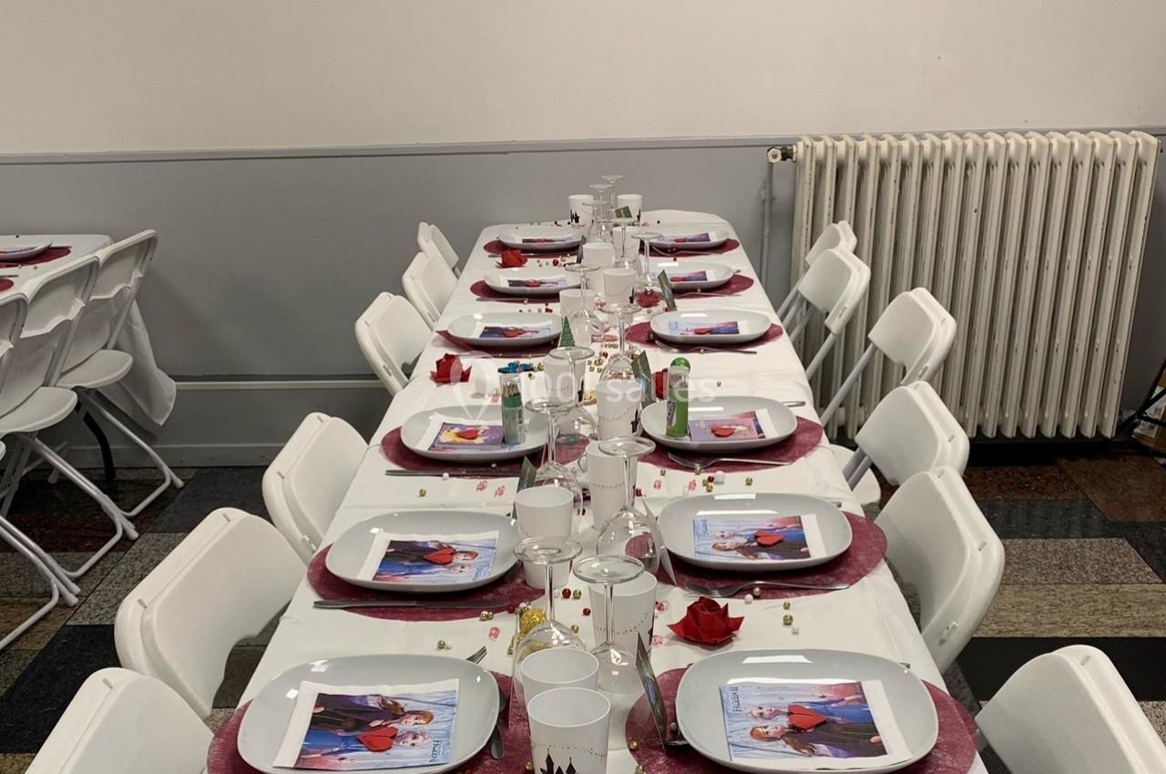Table dressée avec des assiettes décorées, nappes blanches, pétales rouges et confettis, dans une salle sobre.